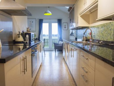 A kitchen with countertops cabinets a sink and a dining area with a chair and glass doors at Our Story Cottage in Longhoughton