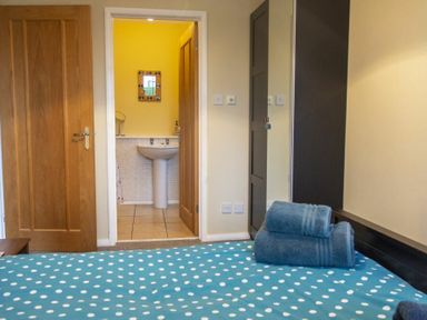 A bedroom with a bed dressed in blue polka dot bedding next to a door leading to a bathroom with a sink at Our Story Cottage in Longhoughton