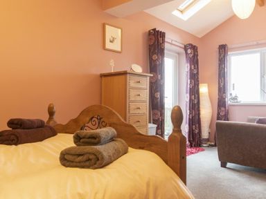 A bedroom with a wooden bed with folded towels a chest of drawers floral curtains and a chair at Our Story Cottage in Longhoughton