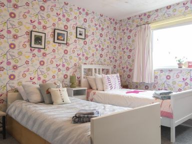 A bedroom with two single beds side by side with floral wallpaper and framed pictures on the wall at Our Story Cottage in Longhoughton