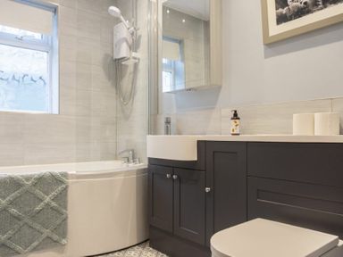 A bathroom with a bathtub shower combination a sink with dark cabinets a mirror and toilet rolls at Our Story Cottage Longhoughton