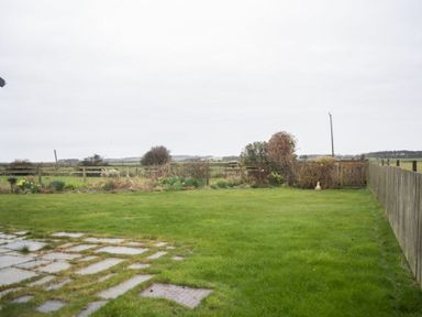 A backyard with grass and stone pathway enclosed by wooden fences at Our Story Cottage in Longhoughton