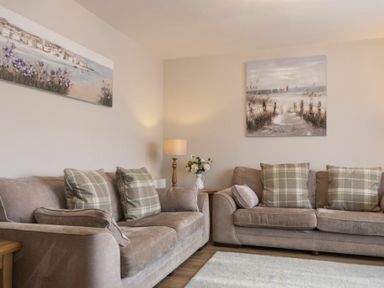 A living room with two beige sofas with plaid cushions a lamp and flower vase on a wooden table at Southfield Lodge in Seahouses