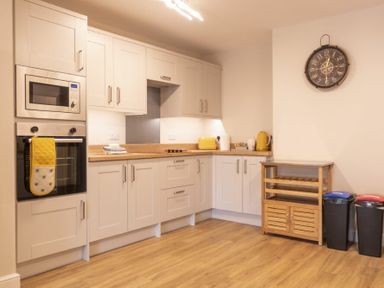 A kitchen with white cabinets wooden countertop microwave oven and clock on the wall at Southfield Lodge in Seahouses
