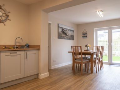 A dining area with wooden table and chairs beside a kitchen sink and cabinets at Southfield Lodge in Seahouses