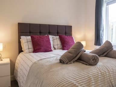 A bedroom with a bed with checked bedding and purple cushions with rolled grey towels on the bed at Southfield Lodge in Seahouses