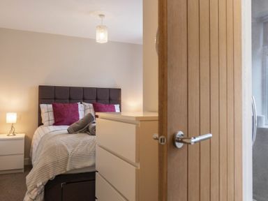 A bedroom with a bed with patterned bedding and purple pillows a bedside table with a lamp and a chest of drawers at Southfield Lodge in Seahouses