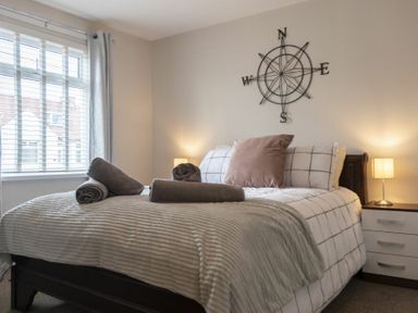A bedroom with a bed made with pillows and folded towels bedside tables with lamps and a compass wall decoration at Southfield Lodge in Seahouses