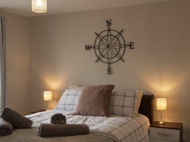A bedroom with a bed with checked bedding two bedside tables with lamps and a compass wall decoration at Southfield Lodge in Seahouses