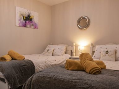 A bedroom with two single beds each with white bedding and bee-themed pillows at Southfield Lodge in Seahouses