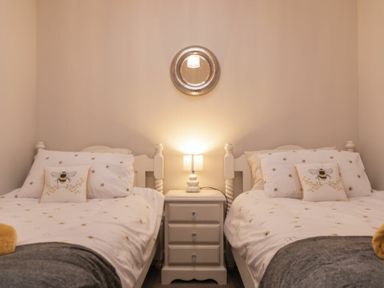 A bedroom with two single beds pillows with bee designs and a nightstand with a lamp in between at Southfield Lodge in Seahouses