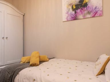 A bedroom with a white wardrobe a bed with yellow towels and bee-themed bedding and a bee artwork on the wall at Southfield Lodge in Seahouses