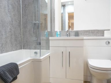 A bathroom with a bathtub with a shower and glass screen a white cabinet with two doors a sink and a toilet at Southfield Lodge in Seahouses