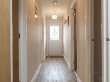 A hallway with wooden doors on both sides and a light fixture above the front door at Southfield Lodge in Seahouses
