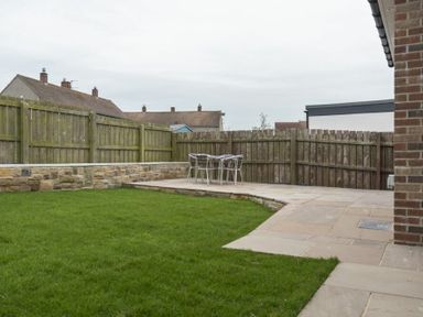 A backyard with green grass a stone patio and metal chairs at Southfield Lodge in Seahouses