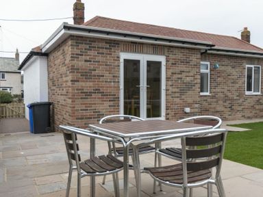 A patio with a metal and wood table and chairs outside a brick building with white double doors at Southfield Lodge in Seahouses