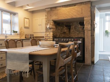 A kitchen with a wooden dining table and chairs and an old stone fireplace at Creel Cottage Craster