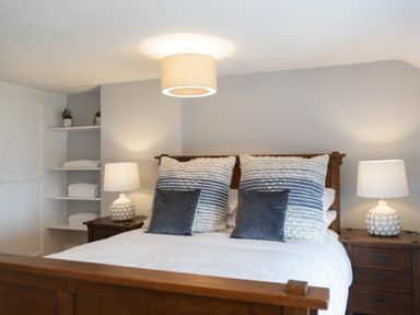 A bedroom with a wooden bed with pillows two bedside tables with lamps and shelves with towels at Creel Cottage Craster