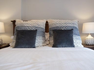 A bed with large striped pillows and smaller dark pillows with bedside tables and lamps at Creel Cottage in Craster