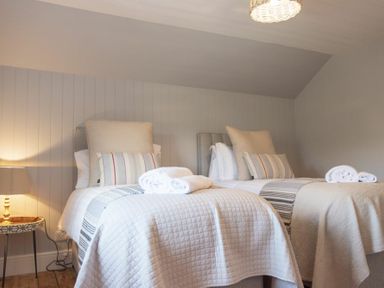 A bedroom with two single beds with striped pillows and rolled towels on each bed at Creel Cottage Craster