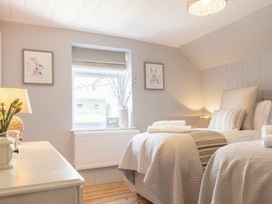 A bedroom with two single beds a window a lamp and framed pictures at Creel Cottage Craster