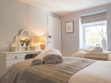 A bedroom with two beds with rolled towels and a dresser with a mirror a lamp and flowers at Creel Cottage Craster
