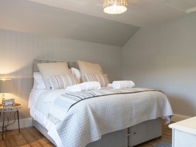 A bedroom with a bed made with white and striped bedding a lamp on a side table and wooden flooring at Creel Cottage Craster