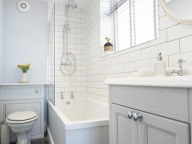 A bathroom with a bathtub shower toilet and sink with tiled walls and a window at Creel Cottage Craster