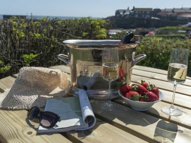 A picnic table with a champagne bucket, two glasses of champagne, a bowl of strawberries, a sunhat, sunglasses, and a map at Creel Cottage in Craster