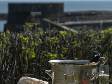 Two glasses of champagne and an ice bucket with a bottle outside near bushes at Creel Cottage Craster