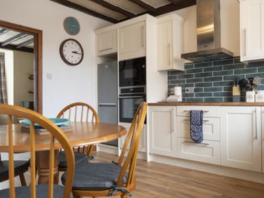 A kitchen with wooden dining table and chairs white cabinets and a stainless steel refrigerator at Kittiwake Cottage Seahouses