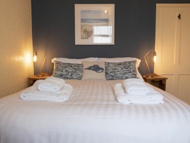 A bedroom with a double bed with folded towels on it and bedside lamps at Kittiwake Cottage Seahouses