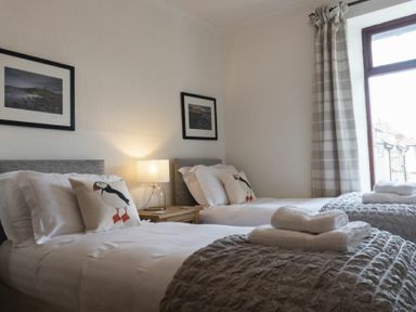A bedroom with two single beds with white linens and puffin pillows at Kittiwake Cottage Seahouses