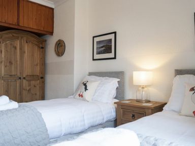 A bedroom with two single beds a wooden wardrobe and a bedside table lamp at Kittiwake Cottage Seahouses