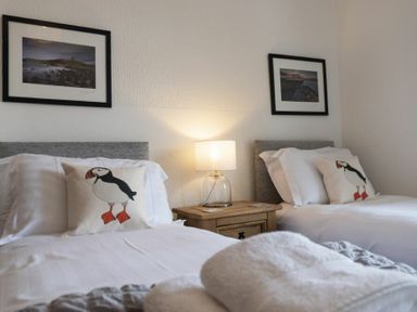 A bedroom with two single beds and a nightstand with a lamp at Kittiwake Cottage Seahouses in Seahouses