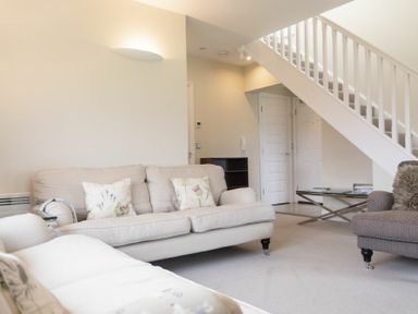 A living room with beige sofas and a glass coffee table under stairs at Keepers View in Bamburgh