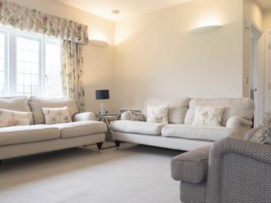 A living room with two beige sofas with floral cushions a window with floral curtains and a grey armchair at Keepers View in Bamburgh