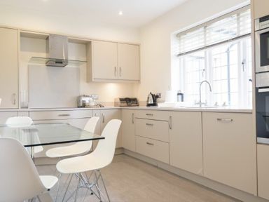 A kitchen with beige cabinets a glass dining table and white chairs at Keepers View in Bamburgh