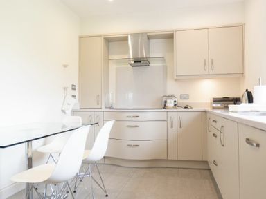 A kitchen with white chairs and a glass table and beige cabinets at Keepers View in Bamburgh