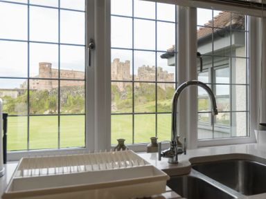 A kitchen sink with dish rack and faucet with a view of a castle through the window at Keeper's View in Bamburgh