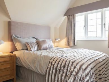 A bedroom with a bed with pillows and a blanket next to a window and wooden nightstand at Keepers View in Bamburgh