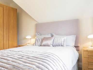 A bedroom with a bed with cushions and a blanket bedside tables with lamps and a wooden wardrobe at Keepers View in Bamburgh