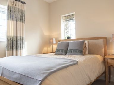 A bedroom with a bed featuring two gray pillows and a blue blanket by windows with curtains and a small plant at Keeper's View Bamburgh