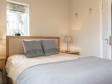 A bedroom with a bed with pillows and a blanket bedside tables lamp and a window at Keepers View Bamburgh