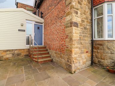 An exterior corner of a building with stone and brick walls a blue door with steps and a metal handrail at The Beach House in Alnmouth