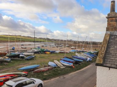 A harbor with multiple sailboats and small boats on the shore next to a road and a building at The Beach House in Alnmouth