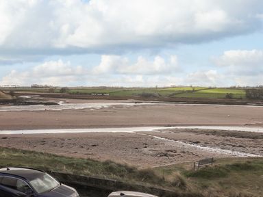 A sandy estuary with water channels and farmland in the background near parked cars at The Beach House in Alnmouth