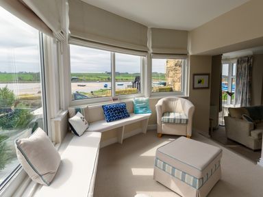 A seating area with window seats, cushions, an armchair, and an ottoman overlooking a waterfront at The Beach House, Alnmouth