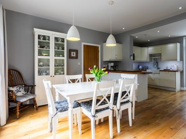 A kitchen with white cabinets a dining table with six chairs and a glass cabinet with dishes at The Beach House Alnmouth