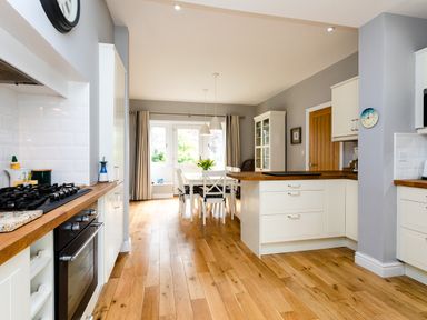 A kitchen with wooden floors white cabinets a dining table with chairs and a glass cabinet at The Beach House Alnmouth